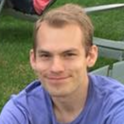 Profile photograph of a smiling young man in a blue T-shirt, seated outdoors